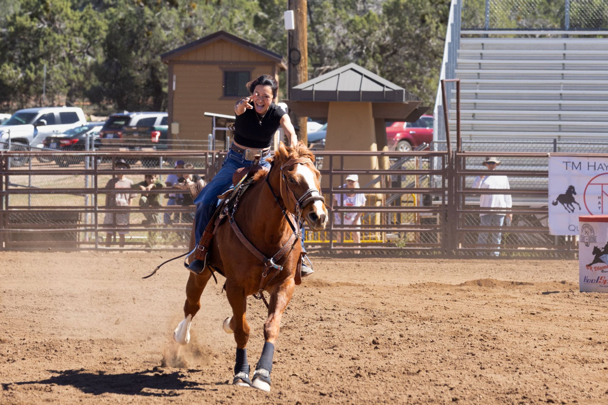 The owner mid-run at a barrel race, pointing at the camera from the saddle of her chestnut quarter horse